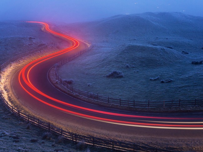 Light trails at the famous winding Mam Nick road below Mam Tor. Temperature: -5 with freezing fog. Derbyshire, Peak District National Park. This is an image I’ve had in mind for a long time now but have been waiting for the right conditions. It was absolutely freezing sat waiting for the cars to come by, every blade of grass was covered in thick frost and I could barely see anything in the thickest patches of drifting fog. Everything came together in the end though, and after capturing a few light trails I headed back home to the warmth. ABOUT MAM TOR: Mam Tor is a 517m hill near Castleton, in the High Peak area of the Peak District National Park. The hill gets its nickname ‘The Shivering Mountain’ from the frequent landslips that occur on the eastern face of the hill, caused by unstable layers of shale. At the base of Mam Tor and at nearby Winnats Pass are four famous caverns where semi precious minerals such as Blue John were once mined. These caverns are known as; the Blue John Cavern, the Peak Cavern, the Speedwell Cavern, and the Treak Cliff Cavern.