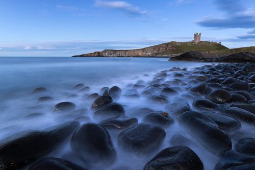 Classic view of the black Embleton boulders looking towards the imposing shape of Dunstanburgh Castle. After photographing the sunrise at Craster we decided to visit the famous viewpoint at Embleton for the blue hour.