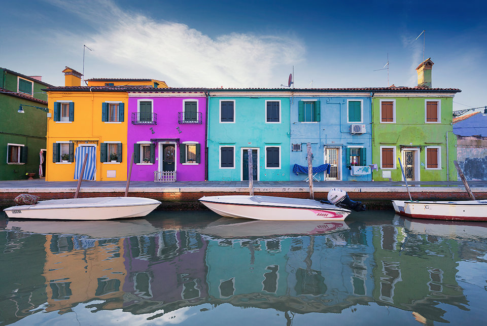 Colourful Burano houses reflected in one of the many picturesque canals running through the historic streets. We visited Burano on a beautifully sunny clear blue sky day, these conditions are not always best for photography, but the bright blue sky added another variation of colour to the multicoloured Burano houses. 
